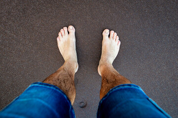 In the photo, feet are visible on a black sand beach in Madeira, where the dark sand contrasts with...