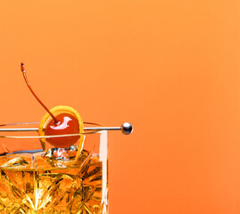 Classic old fashioned cocktail with cherry and orange peel garnish on vibrant orange color background. Alcoholic drink close-up and room for menu text.