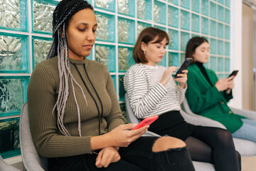 Carefree multiethnic casual young people sitting in lobby of civil service building browsing web...
