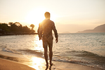 Man, walking on beach and ocean with sunset, lens flare with back view and waves on vacation in Hawaii. Tourism, travel and adventure with peace, zen and fresh air for wellness, summer and sunshine