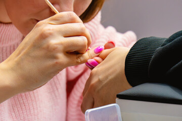 A makeup artist does a manicure on the nails of his client. Her gaze is attentive and focused on her work.