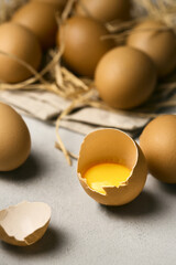 Raw eggs on a grey background  with one broke egg on a straw pillow, easter concept