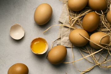 Raw eggs on a grey background  with one broke egg on a straw pillow, top view