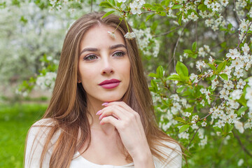 Beautiful fashion model with long brown hair and natural makeup against floral background outdoor - 768592290