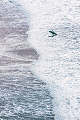 Aerial view of the beach shore with the silhouette of a surfer with his board coming out of the water

