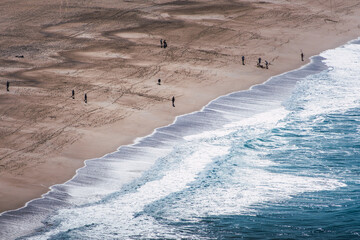 Aerial view of the beach shore with silhouettes of people walking along the shore
