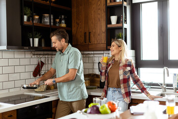 Man and woman sharing a laugh as they cook in a cozy, well-organized kitchen - 768598057