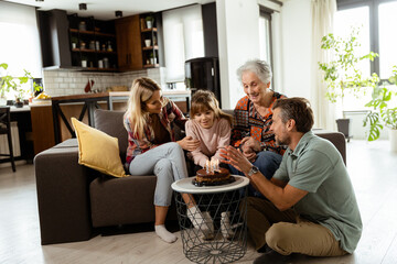 Joyous Family Celebrating Grandmothers Birthday With Cake in a Cozy Living Room - 768598288