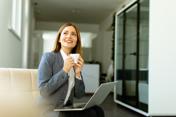 Elegant businesswoman enjoying a peaceful coffee break on sunny office morning - 768598401