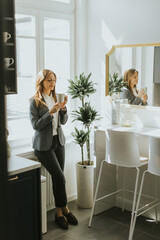Businesswoman enjoying a morning coffee break in a sunlit modern kitchen - 768598677