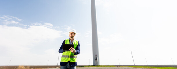 Engineer Inspecting Wind Turbine Efficiency in Vast Green Field on a Sunny Day. - 768598879