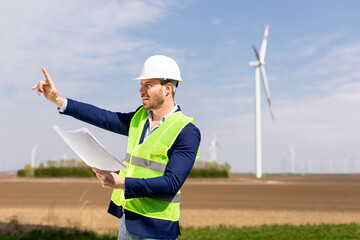 Smiling Engineer Reviewing Plans Near Wind Turbines on a Sunny Day. Generative AI - 768599081