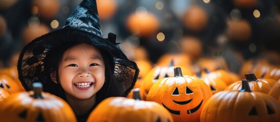 A young girl wearing a witchs hat stands amidst a group of pumpkins, embodying the Halloween spirit. She is dressed in a black witch costume, ready to celebrate the holiday with festive decorations. - obrazy, fototapety, plakaty
