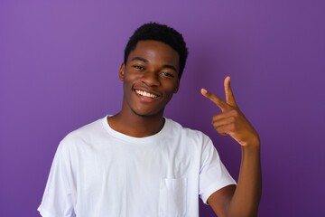 Fototapeta premium African american male person with toothy smile on face pointing with index finger on empty space over violet background. Handsome young guy indicating place for advertising text in studio