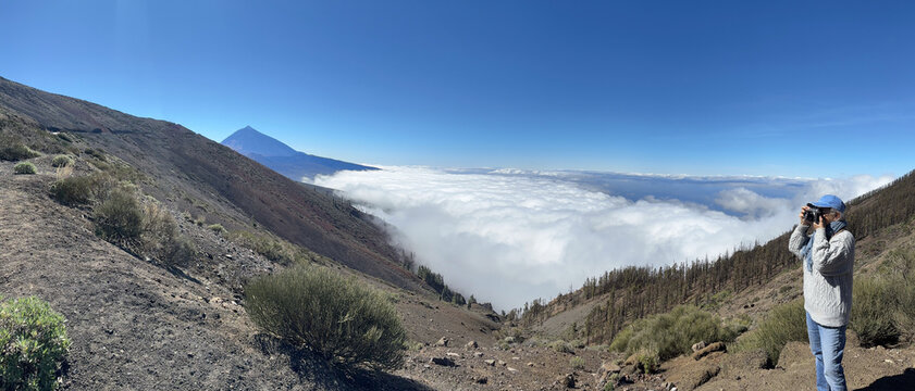 Woman tourist visiting the island of Tenerife takes photographs from the top of the mountain above a sea of clouds, in the distance rises the Teide volcano