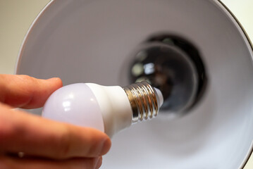 Close up of menhand holding LED light bulb, going to place in into the lamp. Upgrading your home's lighting with energy-efficient light bulb