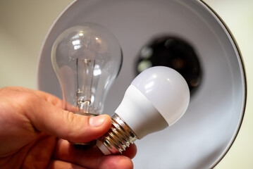 Men`s hand holding two light bulbs, one incandescent, the other LED, close up. Replacing old light...