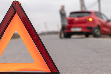 Red triangle of a stopped car on the road. Woman calling for assistance after breaking down with...