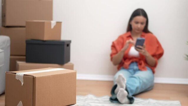 A young, joyful woman embraces moving day in her new home, surrounded by carton boxes, happily engaged in a video call with friends