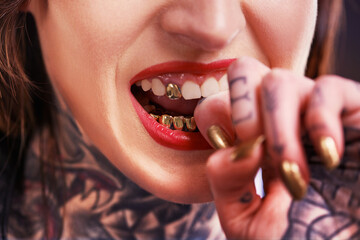Woman, bite and hand with tattoo and nails for grill on tooth and ink design for creative and unique. Art on skin for bold and cool for statement and funky for trend, gold and pattern with red lips - obrazy, fototapety, plakaty