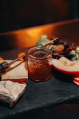 Sliced cheese, a jar of honey and pieces of apples on a wooden stand