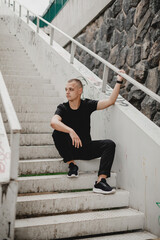 A man in a black shirt sits on a set of stairs. The stairs are white and the man is leaning against them