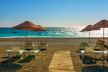 beautiful pebble beach and emerald water. sun lounger and straw umbrella on a deserted beach. Mediterranean coast.
