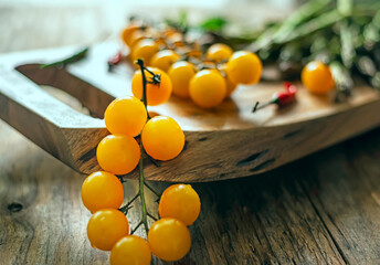 branch with yellow cherry tomatoes on a wooden board and other vegetables in the background out of focus