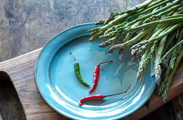 asparagus and hot colorful peppers on a blue plate on a wooden board.
