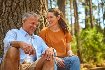 Retired Senior Couple Taking A Break Sitting At Base Of Tree On Hike Through Countryside - 768623869