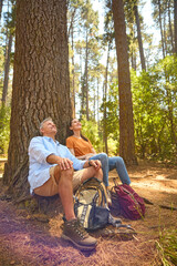 Retired Senior Couple Taking A Break Sitting At Base Of Tree On Hike Through Countryside - 768628491