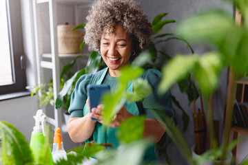 Mature mixed race smiling woman gardener working in home garden, using a smartphone
