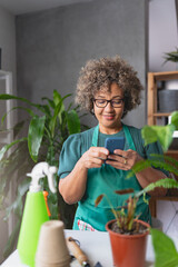 Mature mixed race smiling woman gardener working in home garden, using a smartphone