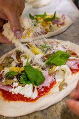 Pizzaiolo mentre guarnisce una pizza tradizionale napoletana con del formaggio grattugiato prima di infornarla