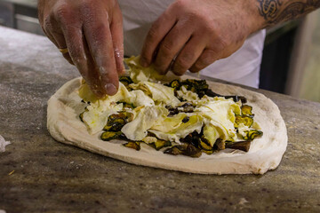 Pizzaiolo mentre condisce una pizza tradizionale napoletana con zucchine fritte e mozzarella di bufala