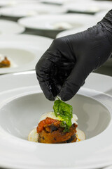 Chef mentre impiatta una Parmigiana di melanzane guarnita con stracciata di bufala e basilico...