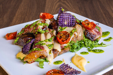 Tagliata di carne cotta al sangue e guarnita con salsa al basilico, pomodori, chips di patate viola...