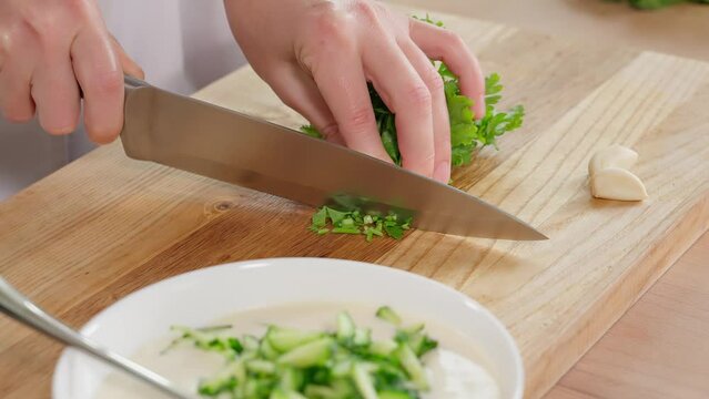 The chef prepares a healthy vegan breakfast. Cuts greens, kale, parsley, cilantro with a sharp knife on a wooden board. Healthy eating, home cooking, diet, diet food, vegetarian food. Close-up, side v