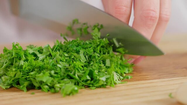 Macro, chef cuts greens, kale, parsley, cilantro with a sharp knife on a wooden board. Healthy eating, home cooking, diet, diet food, vegetarian food. Close-up, front view