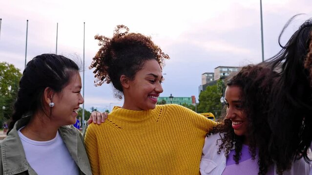 Young diverse group of happy girls laughing together at city street. Female friendship concept with millennial multiracial women hanging out outdoors. Slow motion footage.