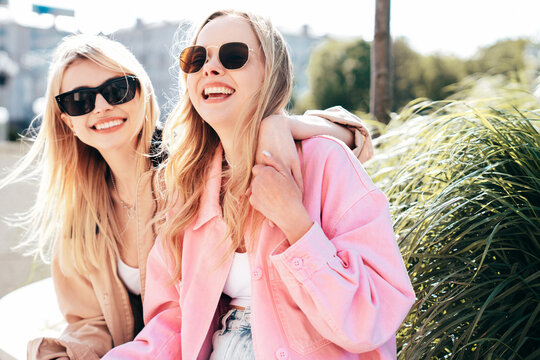 Two young beautiful smiling hipster female in trendy summer clothes. Sexy carefree women posing on street background. Positive models having fun, hugging at sunset. In sunglasses