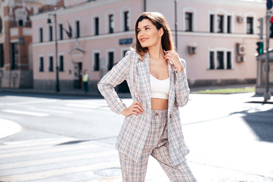 Portrait of young beautiful brunette woman wearing nice trendy plaid suit jacket. Sexy smiling model posing in the street at sunny day. Fashionable female outdoors. Cheerful and happy.