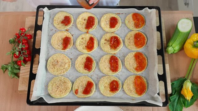 White zucchini slices coated in breadcrumbs and seasonings and topped with tomato sauce. Zucchini dish, zucchini recipe, quick snack. Close-up, top view, fast motion