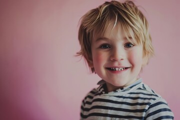 Portrait of a cute little boy smiling on a pink background.