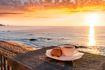 Fototapeta na wymiar concept of street outdoor breakfast with a cup of tea or coffee on a morning coast during sunrise. landscape of city embarkment with sea water and cloudy sky on background