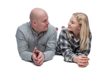 Dad and adult daughter smile and look at each other. A bald man in a gray shirt and a pretty blonde teenager in a black and white checkered shirt are lying on the floor. 