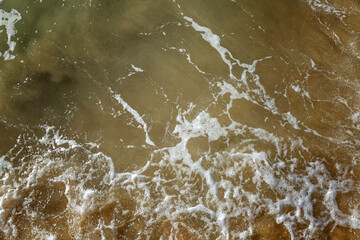 Foamy sea wave on the sandy shore. Muddy dirty green water surface. Top view. Background. Space for text.