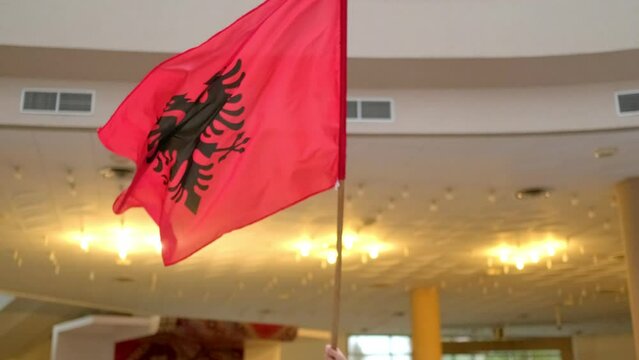 The Albanian flag sways with pride indoors, a symbol cherished, never hide