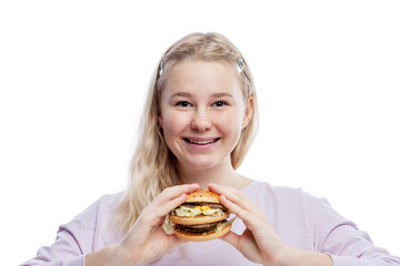 Smiling young girl with a big hamburger in her hands. Cute blonde teenager with freckles in a pink sweater. Delicious garbage food. Isolated on a white background.
