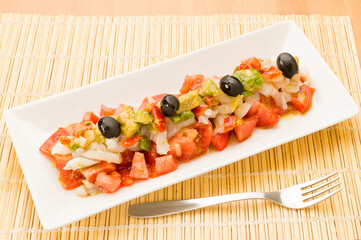 Spanish salad on a plate next to a fork on the table.